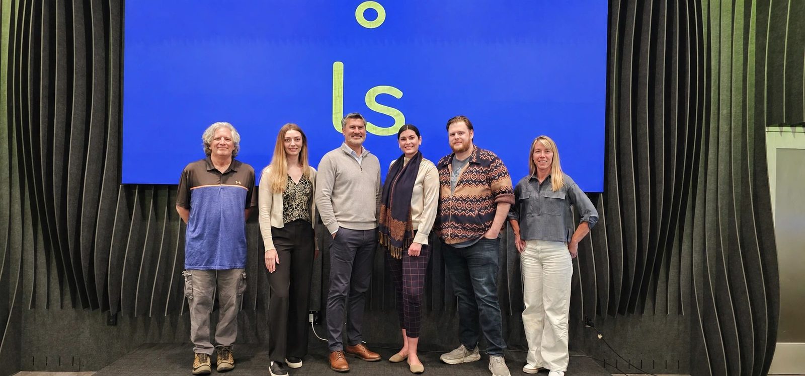 The six members of the Lucidity Sciences team standing together in front of a screen showing the ls mark